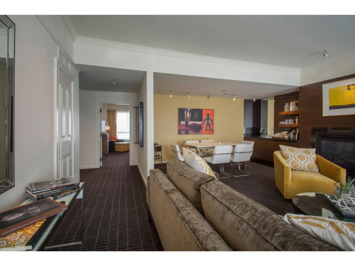 A contemporary living and dining area with a plush sofa, vibrant yellow chair, art-adorned walls, and an inviting dining table. The space feels open and welcoming, ideal for both entertaining guests and cozy nights in.