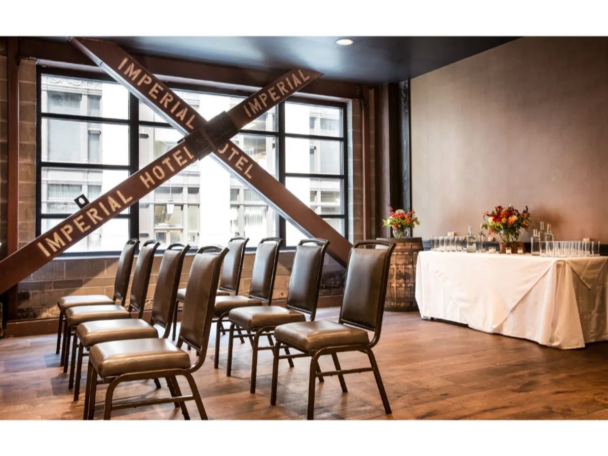 A spacious interior with exposed wooden beams featuring the 'IMPERIAL HOTEL' signage, rows of chairs set up for a formal event or seminar, and a decorative table adorned with flowers and glasses, suggesting versatility for both business meetings and celebratory gatherings.
