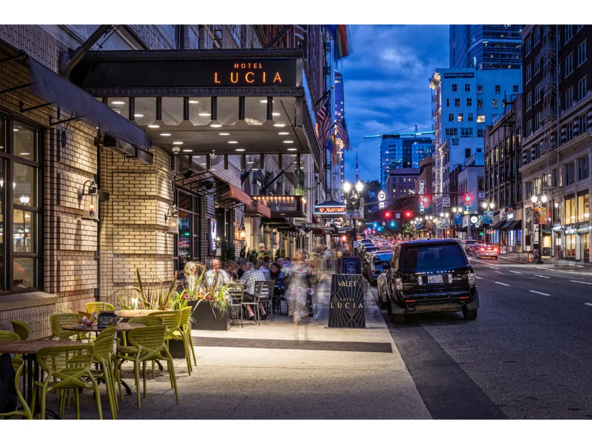 A welcoming outdoor seating area in front of Hotel Lucia is set aglow under city lights, with people dining and socializing. The Hotel Lucia sign is visible, connecting the experience directly to the property.