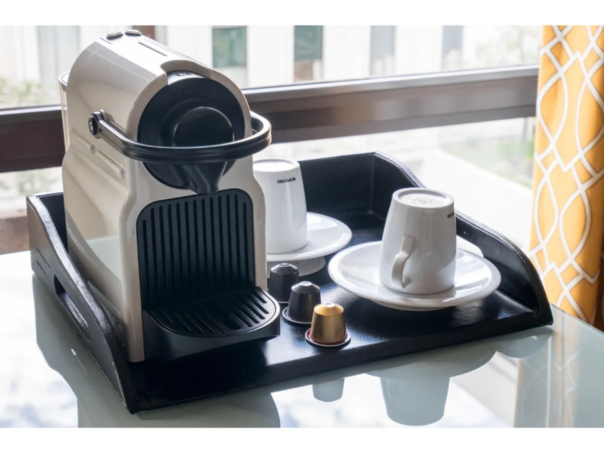 A close-up of a coffee machine with coffee cups and a tray, set in a cozy interior space. The image exudes warmth and comfort, inviting visitors to personalize their arrival experience with a fresh cup of coffee or tea.
